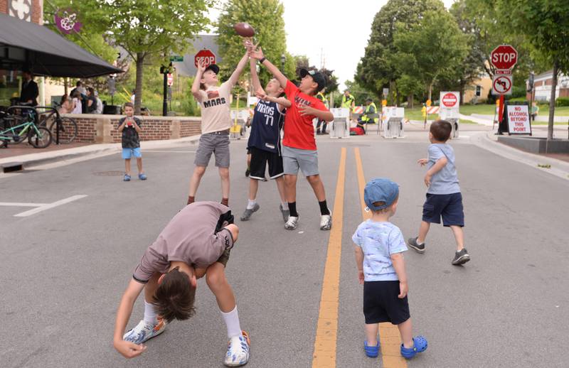 Glen Ellyn children including (front) Cash Condron  and (left-right) Henry Potomis, Henry Aiello and Micah Jacobs play football while a concert is held downtown Glen Ellyn Friday June 8, 2024.