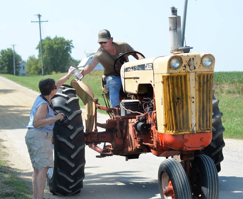 Mary Pretzch of Franklin Grove hands a bottle of water to her son, David, as he drives Paul Erisman's antique Case tractor in the Living History Antique Equipment Association's tractor drive on Saturday.