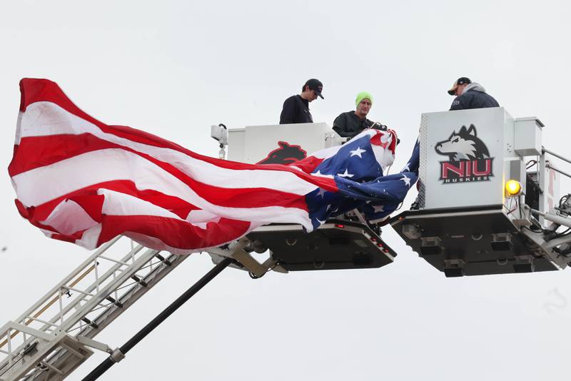 DeKalb and Shabbona firefighters unfurl a large American Flag on DeKalb Avenue in Sycamore Monday, April 1, 2024, that will fly over a processional honoring DeKalb County Sheriff’s Deputy Christina Musil. Musil, 35, was killed Thursday while on duty after a truck rear-ended her police vehicle in Waterman.