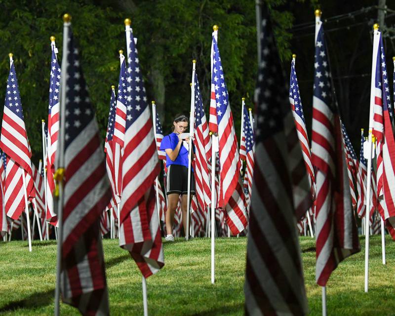 A community member adds names of her family on a dog tag that she placed on one of 500 American flags that are on display to honor veterans, active military, first responders as well as frontline workers on Sunday Sep. 3, 2023, in honor of her family held at Denning Park in La Grange.