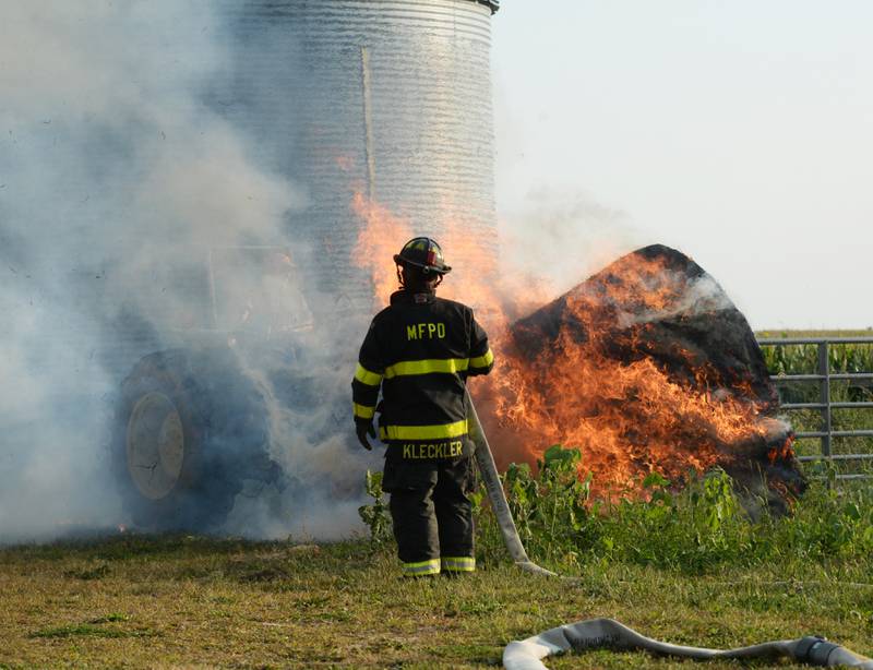 Lyle Hopkins of rural Polo uses a John Deere tractor to move a burning round bale of hay away from a machine shed owned by his neighbor, Herschel Newcomer,  during a Monday evening fire at 7015 W. Judson Road, southeast of Polo on Sept. 10, 2024. Several fire departments assisted the Polo Fire Department on the call. There were no injuries.