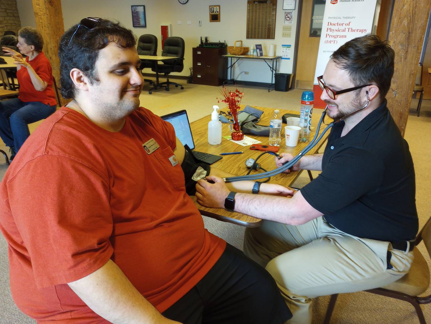 NIU physical therapy student Josh Starner demonstrates a blood pressure check on fellow student Aidan Brown Saturday at the WellBatavia Festival. Several students conducted health screenings, such as speech and language, speech and Batavia's downtown accessibility.
