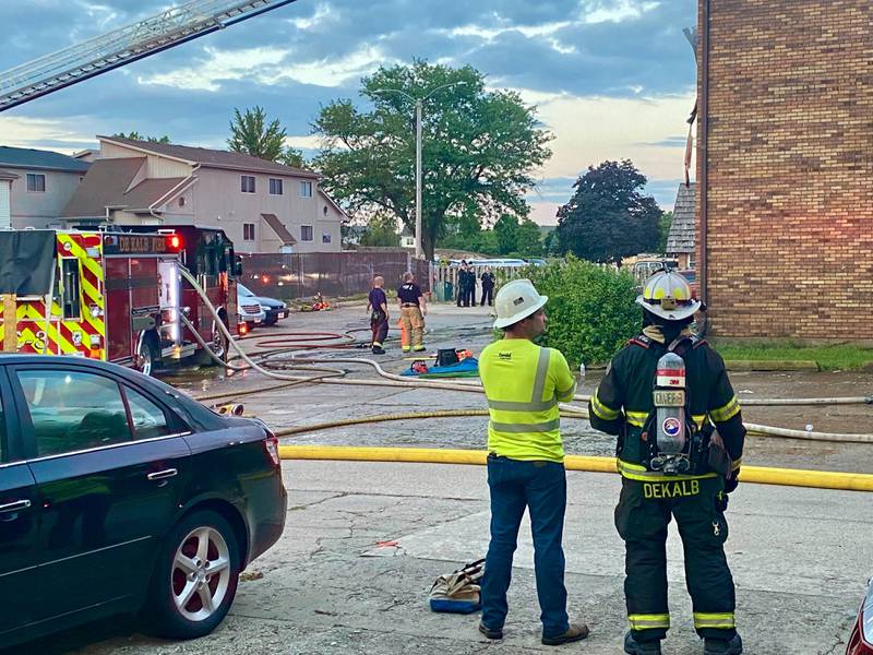Two DeKalb firemen look on as a Rochelle Fire Department ladder truck deploys its crews responding to a structure fire in the rear parking lot of a Husky Ridge apartment complex in the 800 block of Kimberly Drive, DeKalb, on Wednesday evening, May 29, 2024.