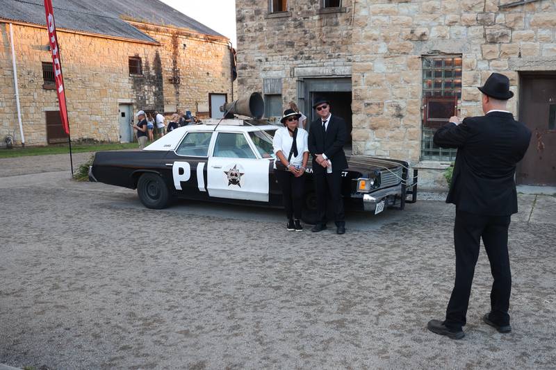 A couple gets their photo taken with the Bluesmobile at Blues Brothers Con: The Sequel on Saturday, Aug. 17, 2024 at the Old Joliet Prison.