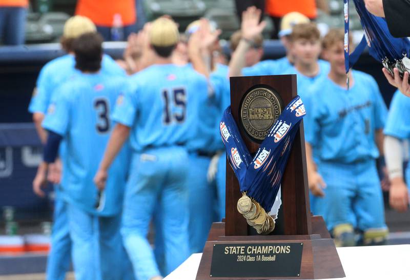 Members of the Marquette baseball team hi-five each other in the background Class 1A State championship trophy on Saturday, June 1, 2024 at Dozer Park in Peoria.