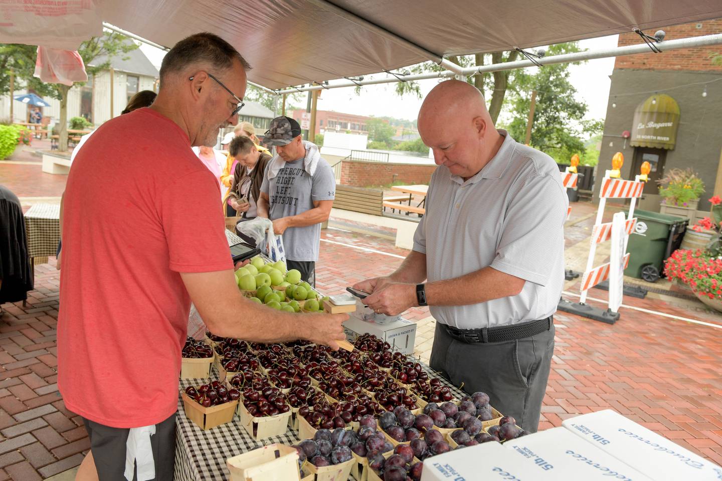 Jason Latham from Flat Tire Farm sells his fresh produce to Kevin Phalen at the Batavia Farmers' Market on Saturday, August 5, 2023.