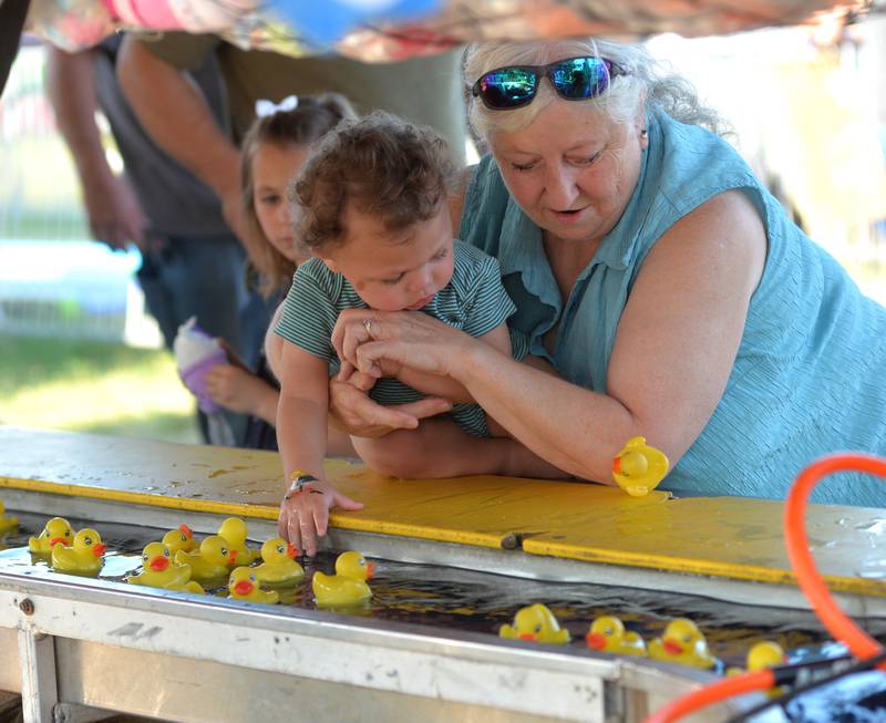 Lauri Johnson helps Michael Burt, 1, of Amboy snare a plastic duck at one of the carnival booths during the Ogle County fair on Saturday, Aug. 5, 2023.