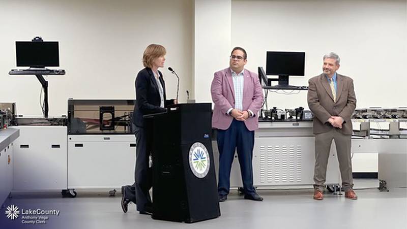 Lake County Board Chair Sandy Hart speaks at the unveiling event while Lake County Clerk Anthony Vega (center) and Valentino Guyett, BlueCrest director of mail operations, looks on.