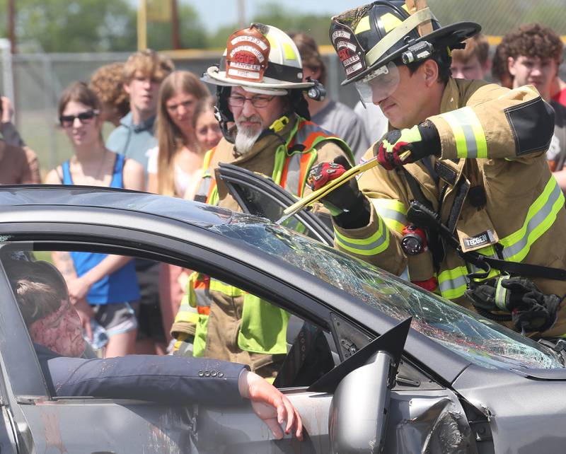 Granville deputy chief Mike Burr and captain Nathan Sons use tools to cut glass out of the windshield of a vehicle as Putnam County High School student Eric Vipond is trapped inside during a "mock prom" scene through the Putnam County Corner's Awareness Program on Friday, May 3, 2024 at Putnam County High School.  Putnam County Fire and EMS units, PC Sheriff, and OSF Lifeflight crew conducted a drill crash scene. The school's prom is Saturday. The program helps students make good choices on prom night.