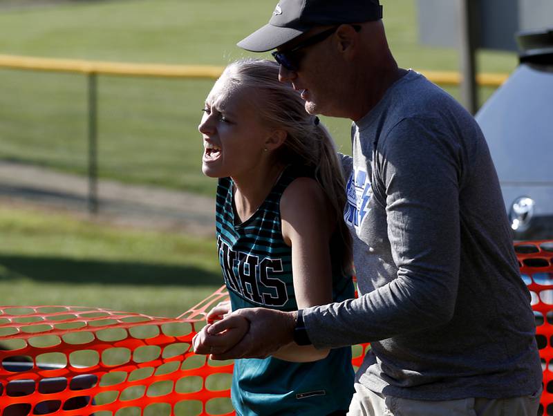 Rob Mecklenburg helps Woodstock North’s Hannah Pittman off the course during the girls race of the McHenry County Cross Country Meet Saturday, August 27, 2022, at Emricson Park in Woodstock.