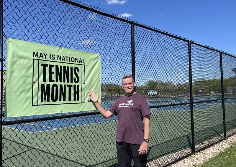 Chris Dudley, Sterling Park District's new Racquetball Sports Director and Head Tennis Professional at Westwood Tennis Center, is posing in front of a green "May is National Tennis Month" sign.