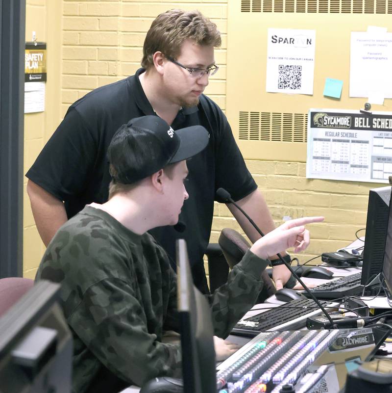 Steven Jamrog, (back) a Spartan TV assistant who is a Sycamore High School graduate, helps freshman Jack Smith as he runs the board during a girls basketball game Friday, Feb. 17, 2023, in the broadcast control room at the school.