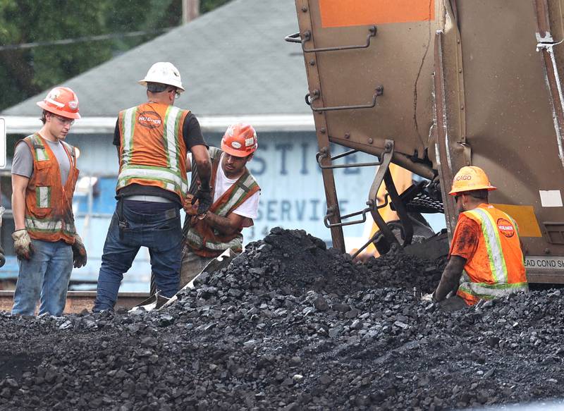 Workers clear debris from the scene of a tipped over coal car after BNSF Railway train traveling east derailed Wednesday, July 10, 2024, on the west side of Somonauk.