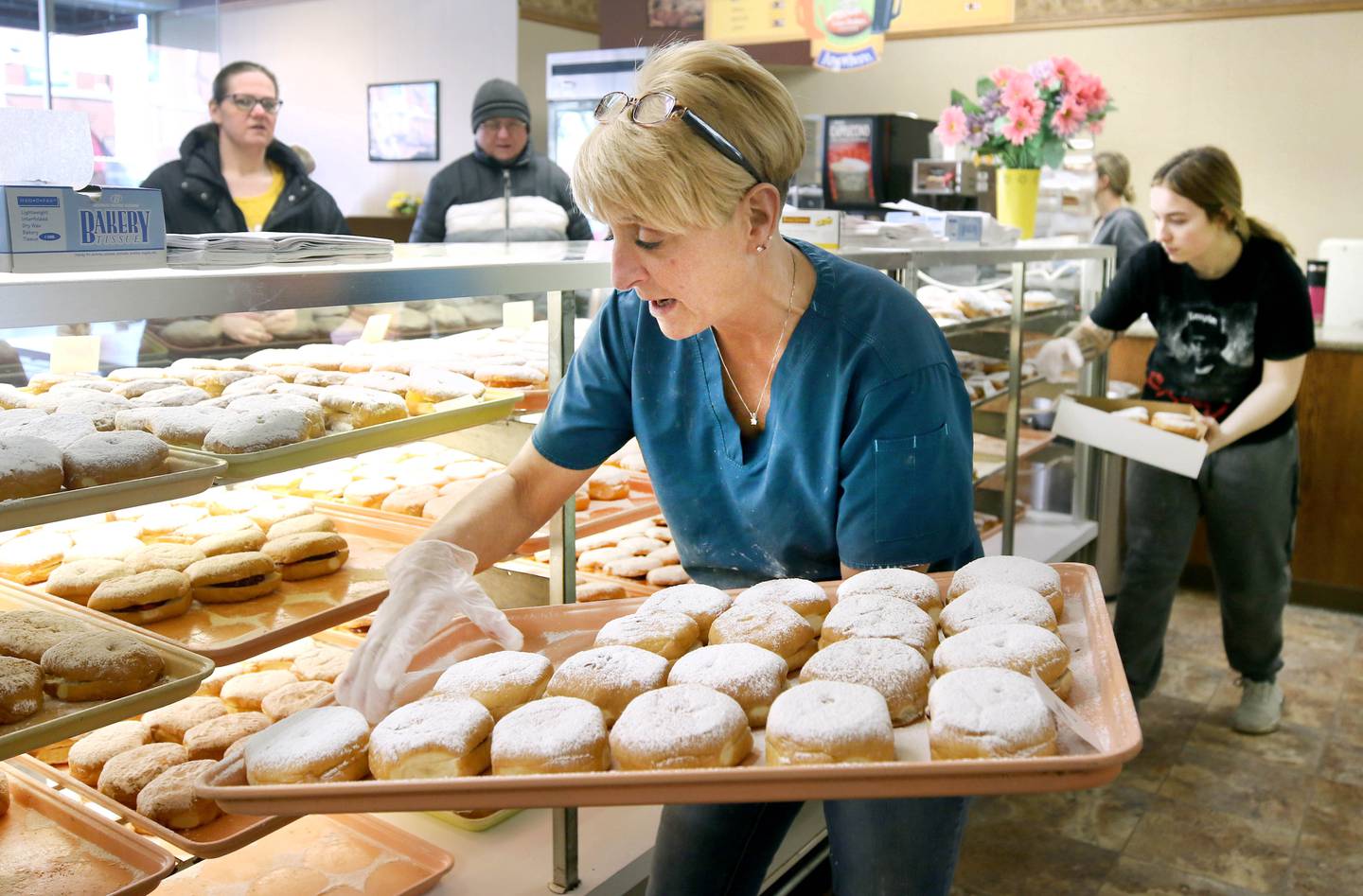 Customers wait in line as Dawn Ekstrom, (left) manager at Elleson's Bakery, restocks the shelves with paczki and employee Zoe Durst fills an order Tuesday, Feb. 21, 2023, at the bakery in Sycamore. Elleson’s is always full of customers on Fat Tuesday, also known as Paczki Day, due to the tradition of enjoying the fried Polish dessert.