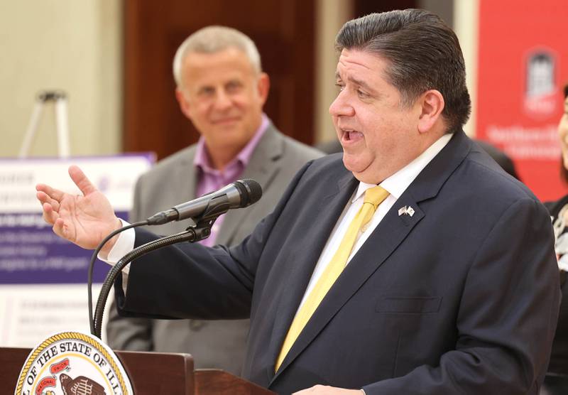 Gov. JB Pritzker, speaks as DeKalb Mayor Cohen Barnes looks on during a news conference Tuesday, April, 4, 2023, in the Barsema Alumni and Visitors Center at Northern Illinois University in DeKalb. Pritzker along with a group of llinois lawmakers, DeKalb city officials and representatives from NIU were on hand to promote the importance of funding higher education in Illinois.