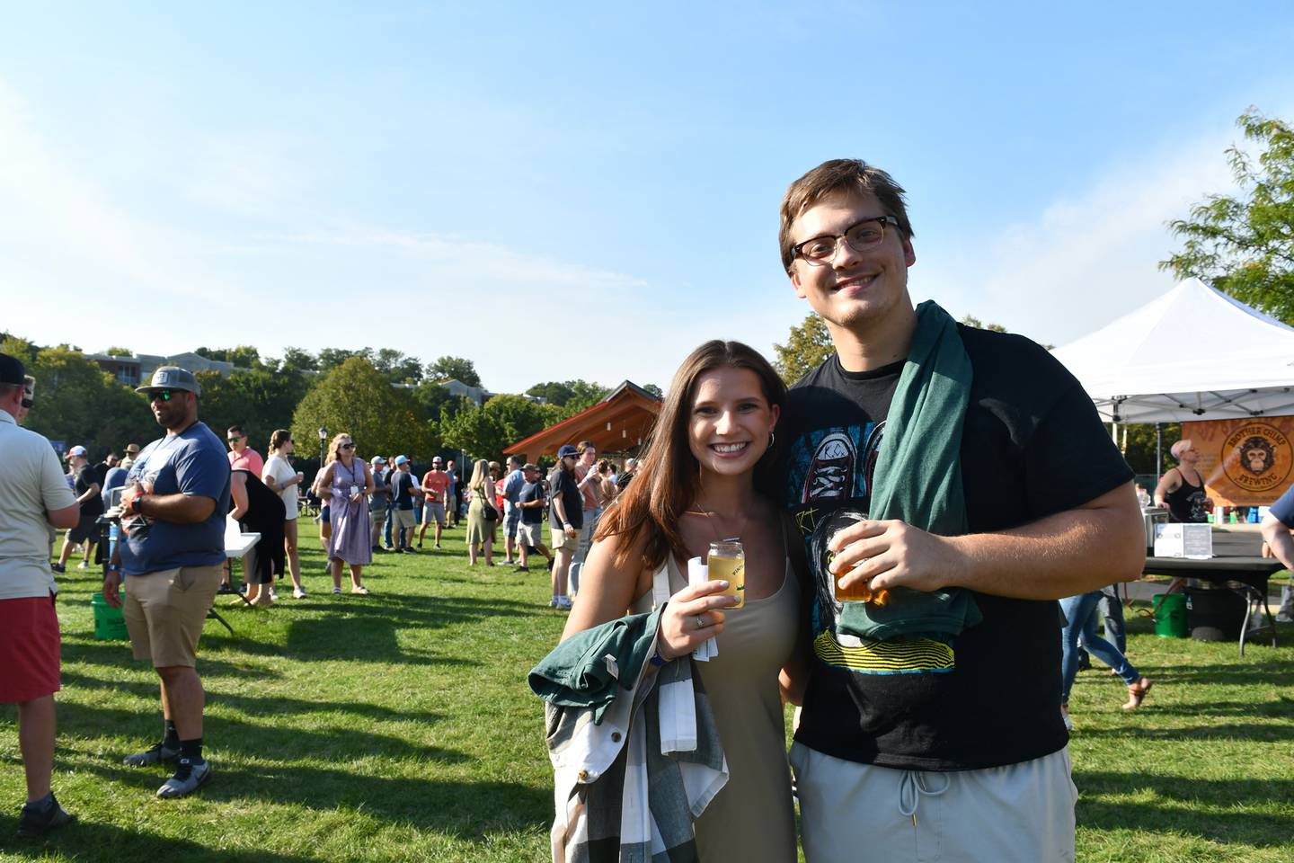 A pair stands together at a past Pints by the Pond festival holding beer-tasting glasses. The 2024 event will feature live music by Prairie Station Acoustic Duo, and food trucks will be on site.