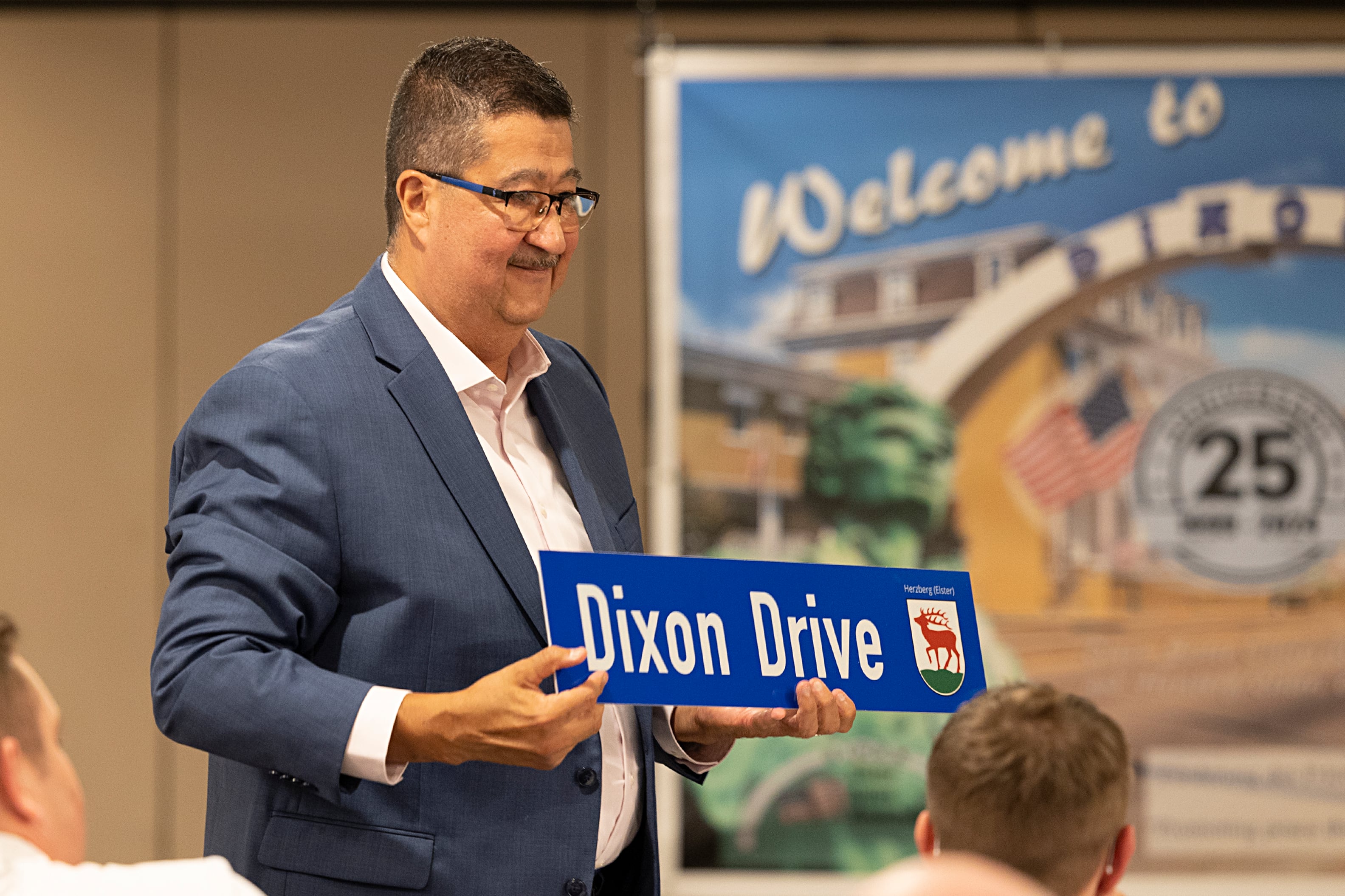 Dixon Sister Cities Association President Steve Caudillo displays one of two signs gifted to the association and the city from Herzberg/Elster Burgermeister Karsten Eule-Pruze Thursday, July 25, 2024. The signs are replicas of ones on display in the town square of Dixon’s German Sister City.