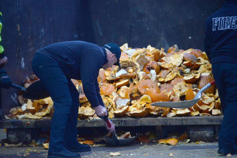 A Byron firefighter scoops up pumpkin pieces and tosses them into a dumpster during  the Byron Fire Department's annual Pumpkin Smashing Event on Wednesday, Nov. 1, 2023.