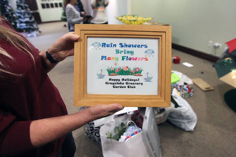 Julie Prentice, of Grayslake holds up the sign which will be next to the Grayslake Greenery Garden Club tree explaining their theme, "Rain Showers Bring Many Flowers, " which will be on display for the Giving Trees exhibit at the Grayslake Heritage Center & Museum.