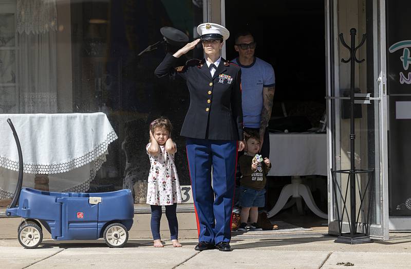 As mom Elise Hume salutes, Andy Mae covers her ears as fire and police vehicles, with their sirens blaring, pass through downtown Dixon on Monday, May 27, 2024. After a ceremony at the riverfront, a group paraded to Oakwood Cemetery for further Memorial Day recognitions.