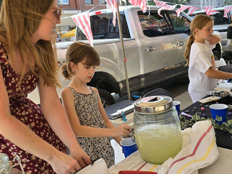 Annabelle Larabee makes an Arnold Palmer for a customer Saturday, Aug. 24, during the third annual Prairie Fox Books Children's Business Fair in downtown Ottawa as her mother Justine watches on and Evie Myers runs the business next to her.