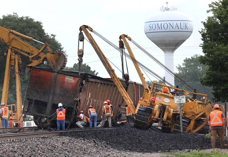 Cranes and a loader upright a tipped over coal car after a BNSF Railway train traveling east derailed Wednesday, July 10, 2024, near Route 34 on the west side of Somonauk.