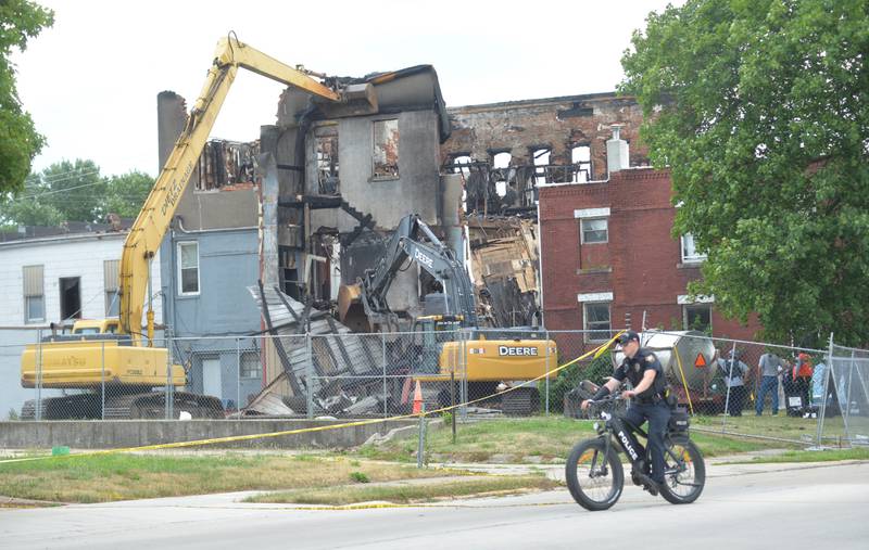 A Sterling police officer on an electric bike patrols the perimeter of a fire scene at 406 E. Third St. in Sterling on Tuesday, July 11, 2023. An excavator removed a portion of the back of the building allowing a search dog to examine debris.