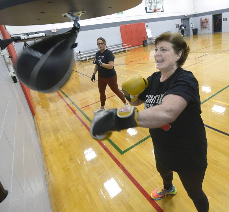 Elaine McKinney punches a boxing bag during her Rocksteady Boxing course at the Streator YMCA with instructor Nichole Reynolds watching.