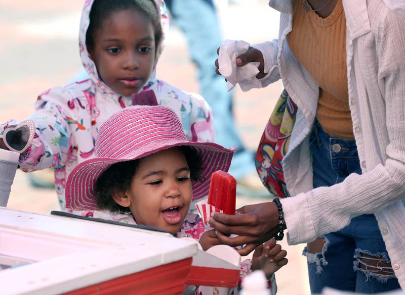 Ellie Thomas, 2, from DeKalb, gets her ice pop from the Ms. Mint’s Pop Shop booth during a very windy opening day at the DeKalb Farmers Market Thursday, June 6, 2024, at Van Buer Plaza in Downtown DeKalb. The market will run from 10 a.m. to 2 p.m. Thursdays through Sept. 19.