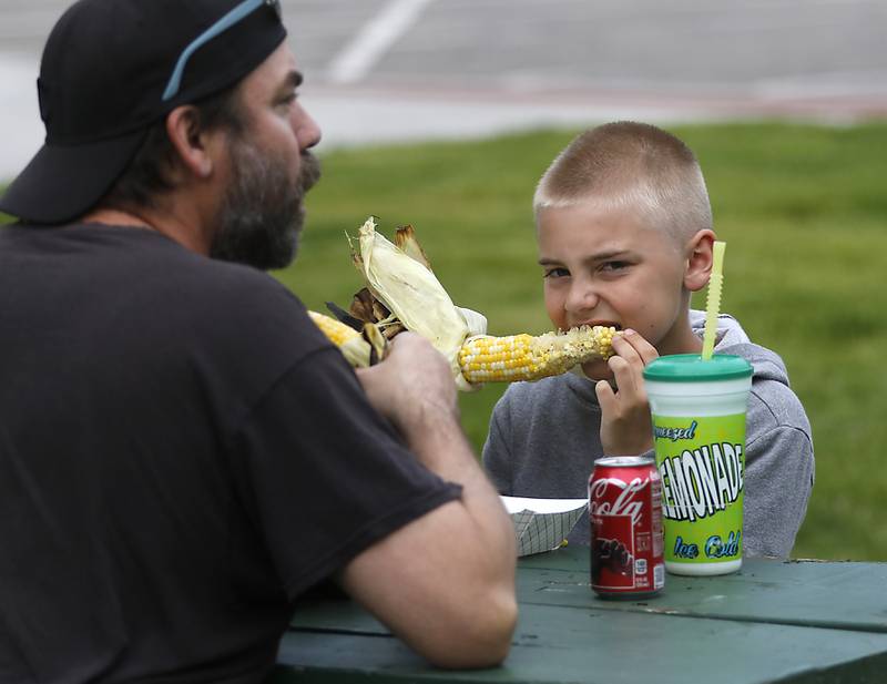 Zachary Kuhns. 9, of McHenry , enjoys a ear of corn while eating with his dad, Jeremy, on Thursday, May 16, 2024, during McHenry's Pearl Street Market and concert at Veteran's Memorial Park. The market features around 35 venders and live music on Thursdays through Sept. 19.