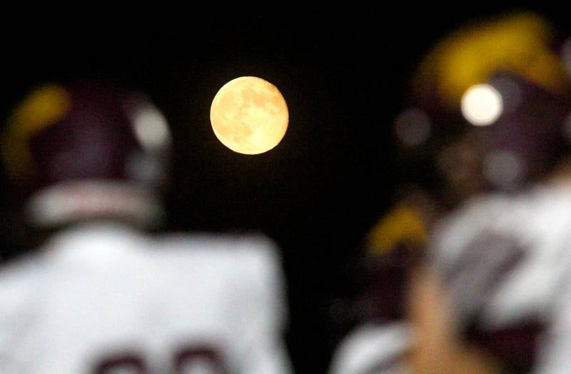 The moon rises as Richmond Burton’s Rockets warm up for varsity football at Rod Poppe Field on the campus of Marengo High School in Marengo on Friday, Oct. 18, 2024.