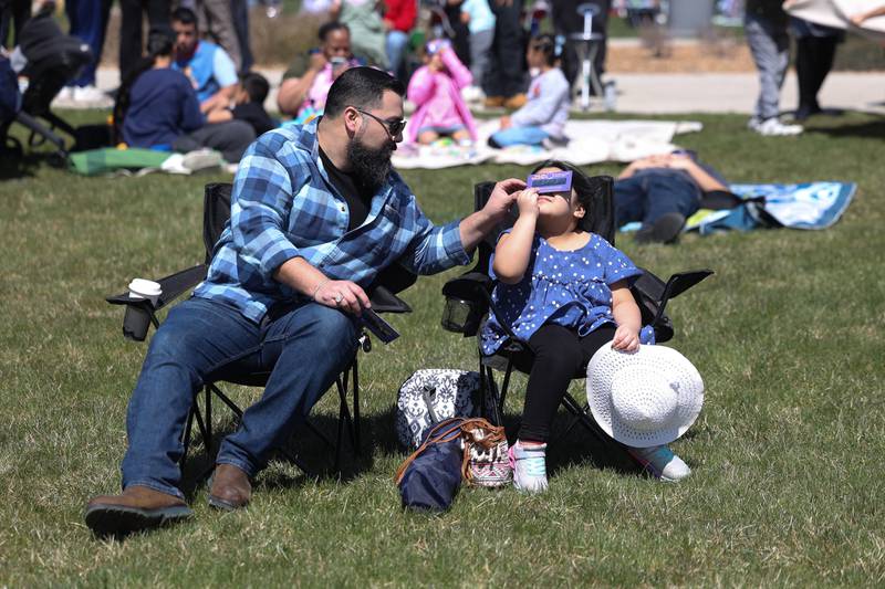 Cesar helps her daughter Lex, 5, with the special glasses to view the eclipse at the Joliet Junior College solar eclipse viewing event on Monday, April 8, 2024 in Joliet.