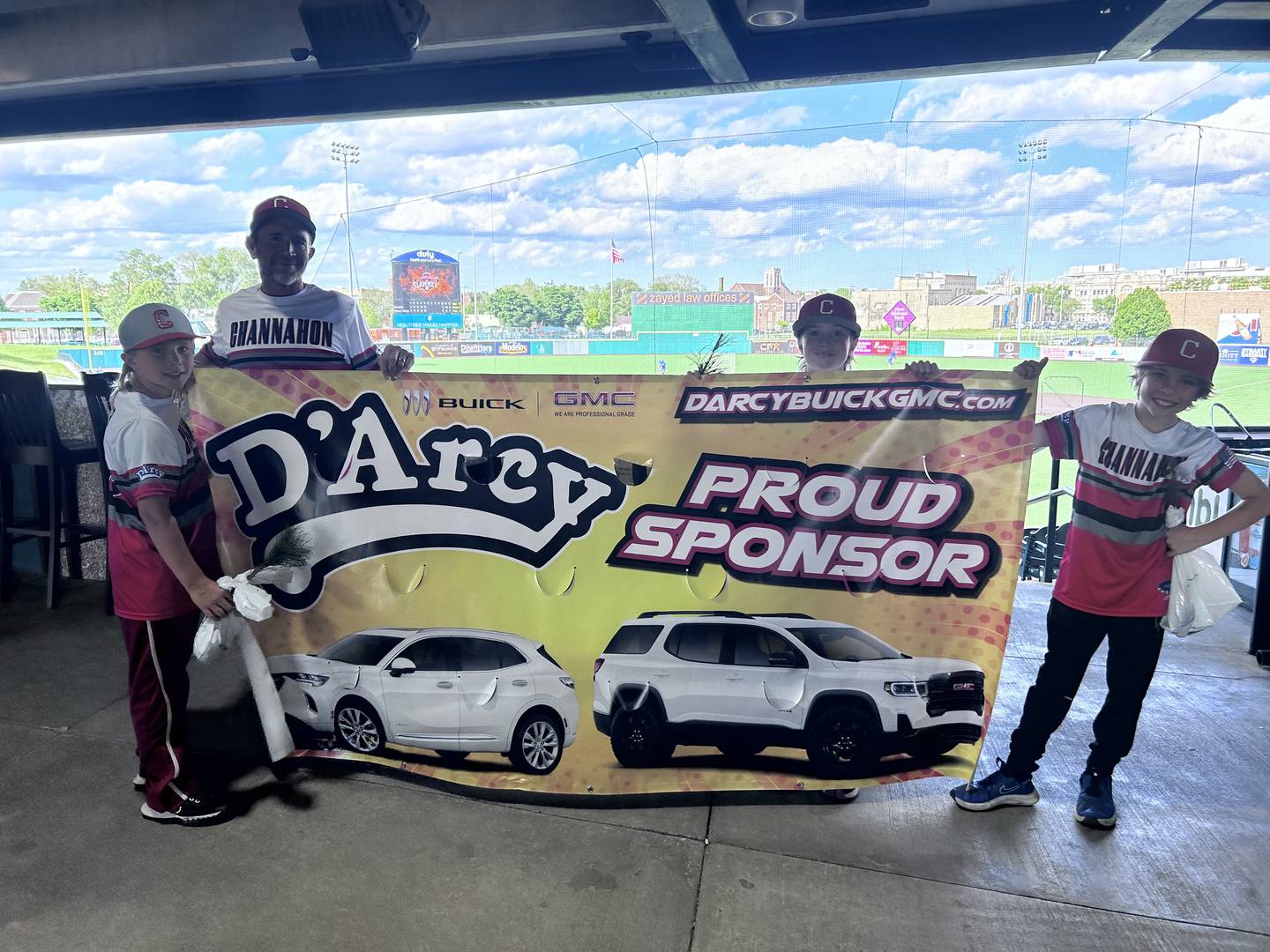 Channahon Mustangs Little League players stand with a banner from tree giveaway sponsor D'Arcy Buick-GMC.