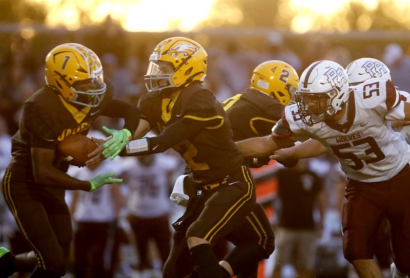 Jacobs' Connor Goehring hands the ball offf to running  back Tyvon Boddie as Prairie Ridge's Jose Esparza reaches for Goehring during a Fox Valley Conference football game on Friday, Aug 30, 2024, at Jacobs High School in Algonquin.