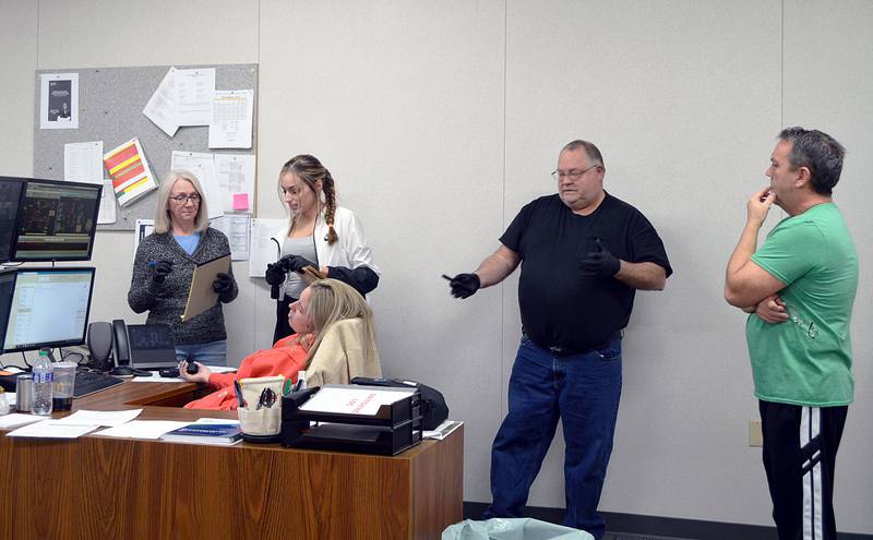Rock Falls Police Department Citizen Police Academy participants Jodi Perez (left) of Rock Falls, Valerie Villaneda of Sterling and Brent Wright of Rock Falls, investigate a mock crime scene with Detective Sgt. Doug Wolber (right) during the group's April 3, 2024, meeting. The "victim" is played by police Officer Autumn Day.