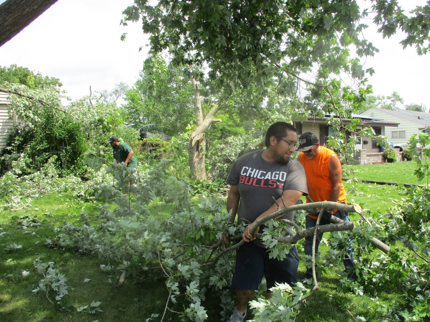 Marycrest neighbors Ruben Barrera (front) Mike Fox (middle) and Israel Ortega (rear) work together to clean up tree limbs at a house in the Joliet subdivision that was hit hard during the Monday night storm. July 16, 2024