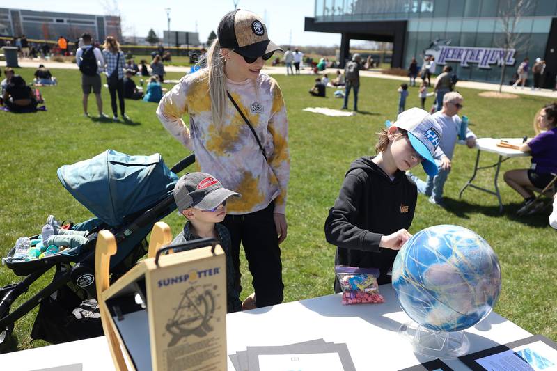 Ashley Egan and her sons Griffin, 5, left and Mick, 9, look at a globe that maps past and upcoming eclipses on display at the Joliet Junior College solar eclipse viewing event on Monday, April 8, 2024 in Joliet.