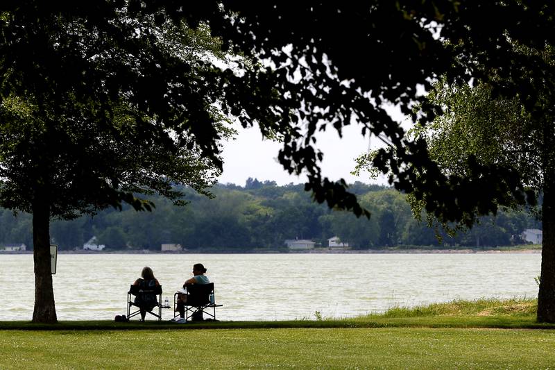 People enjoy a cool breeze as they sit in the shade next to McCullom Lake in Petersen Park on Wednesday, June 19, 2024, in McHenry.