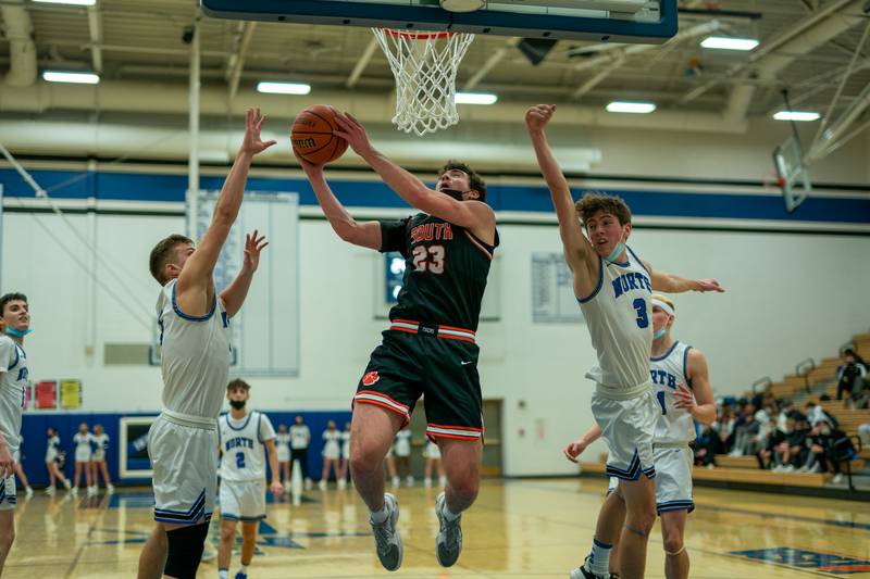 Wheaton Warrenville South's Tyler Fawcett (23) drives to the basket against St. Charles North's Ned Hayes (3) and  Jude Love (5) during a basketball game at St.Charles North High School on Friday, Jan 21, 2022.