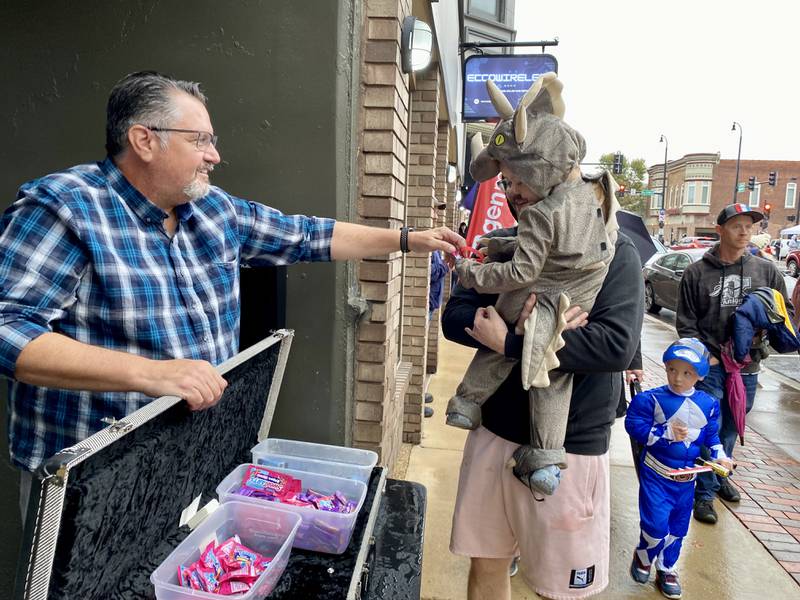 Henry Day, 3, dressed as a Triceratops dinosaur, reaches for some candy outside Aurora Music Company, 137 E. Lincoln Highway, with his dad Jeremy Day, both of Rochelle. Trick-or-treaters swarmed the downtown area Thursday, Oct. 26, 2023 for the 26th annual Spooktacular hosted by the DeKalb Chamber of Commerce.