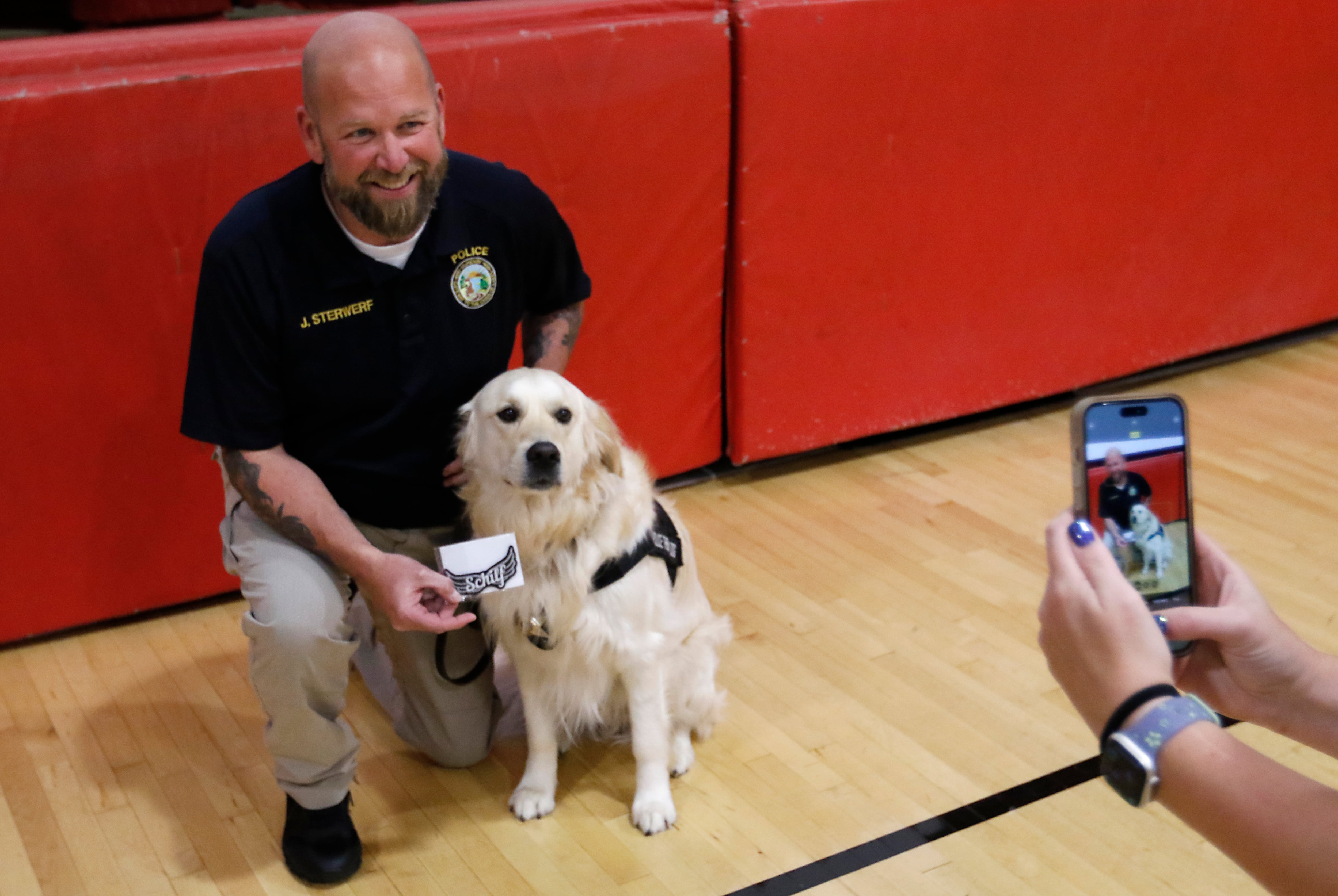 McHenry Police Department therapy dog, Oakley, and McHenry Police Department Social Services Coordinator Jason Sterwerf have their picture taken with the patch honor ing the late teacher Emily Schilf at Duker Elementary School in McHenry on Friday, Aug. 16, 2024.