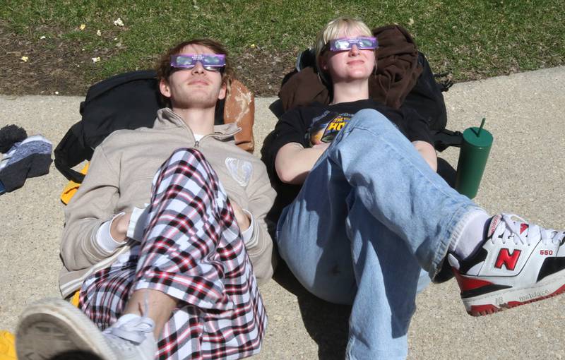 Benjamin Osborn, a Northern Illinois University senior from Rockford, and Emily Claussen, a senior, from McHenry, get comfortable to watch the eclipse progress Monday, April 8, 2024, during the NIU Solar Eclipse Viewing Party behind Davis Hall in DeKalb. Attendees were treated to perfect weather to watch the rare celestial event.