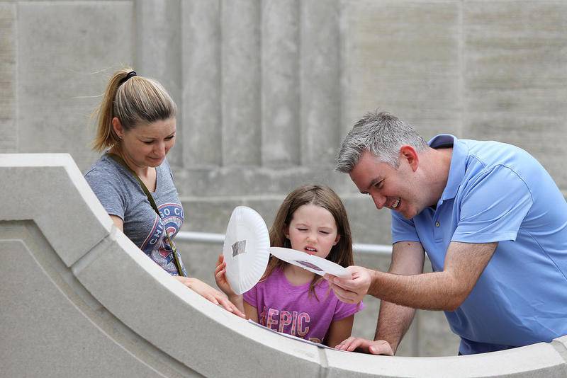 Matthew Apgar - mapgar@shawmedia.com
Jenny Megli (left) watches as husband John (right) uses a pinhole viewer to project an image of the sun onto the structure at the entrance of the DeKalb Public Library for their daughter Lauren, 7, on Monday, Aug. 21, 2017 at the DeKalb Public Library in DeKalb.