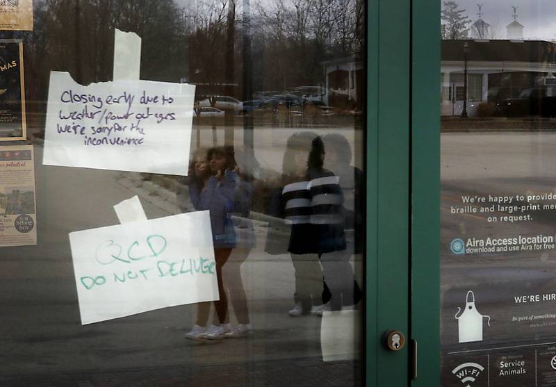 Students walking to the Starbucks in downtown Crystal Lake are reflected in the door where a sign hangs announcing the store is closed due to a weather-related power outage on Thursday, Feb. 23, 2023, as county residents recover from a winter storm that knocked down trees and created power outages throughout McHenry County.