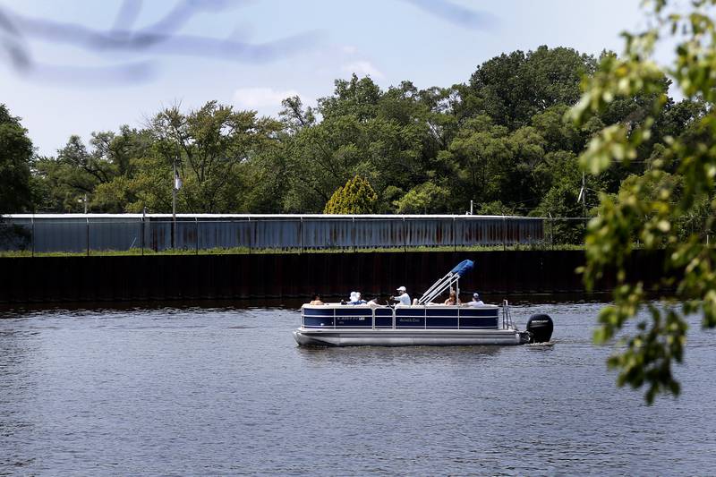 A pontoon boat cruises past the the former wastewater treatment site off Waukegan Road along the Fox River in McHenry on July 12, 2024.  Shodeen Group LLC will present to the McHenry City Council's committee of the whole its plans to develop the site and another downtown location.