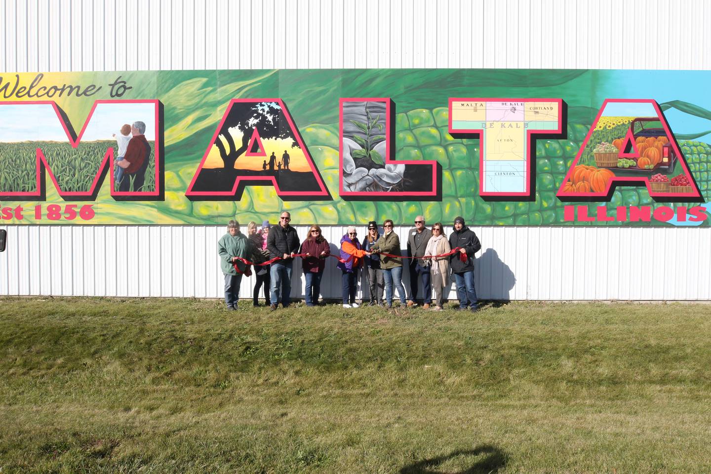 The ribbon is cut by Malta city officials and other people responsible for the completion of the project including Dixon artist Nora Balayti and building owner Shirley Kyler on Wednesday, October 19, 2022, at north side of Route 38 in Malta.  The mural, which spells out Malta in large capital letters, shows the values ​​of the city with themes of agriculture, family, community and growth.