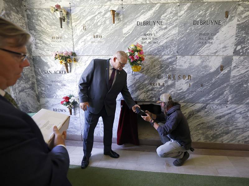 Kane County Coroner Rob Russell, left, hands a box of cremains to St. Charles Township North Cemetery Superintendent Brooks Ronzheimer who then places them in a crypt during a ceremony for the entombment of unclaimed bodies Thursday May 30, 2024 in St. Charles. Funeral Director of Yurs Funeral Homes Timothy Bergman is seen at the far left.