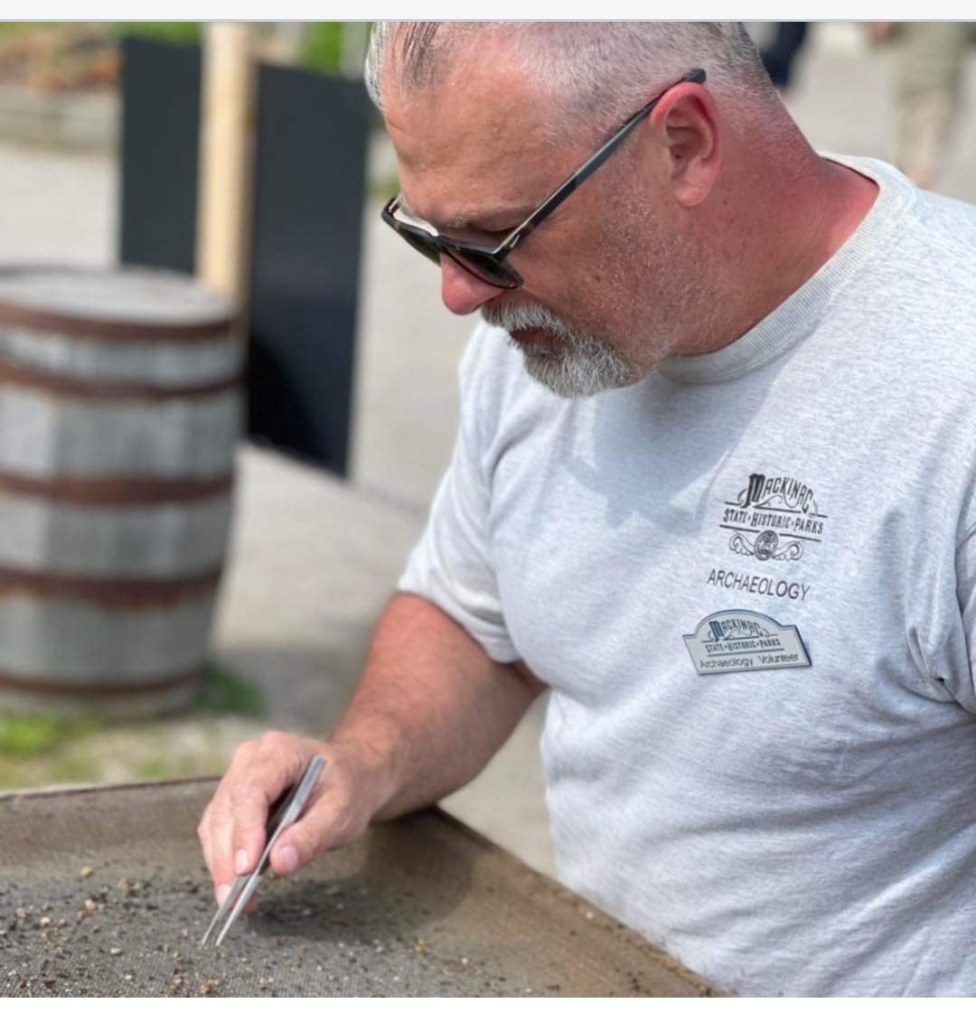 Illinois Valley Community College archaeology professor Jeff Spanbauer picks small finds from a sieve while working at the site of colonial Fort Michilimackinac (Michigan). Drawn to the field by the adventures of fictional archaeologist Indiana Jones, Spanbauer brings his real-life adventures to his classroom where they inspire his students.