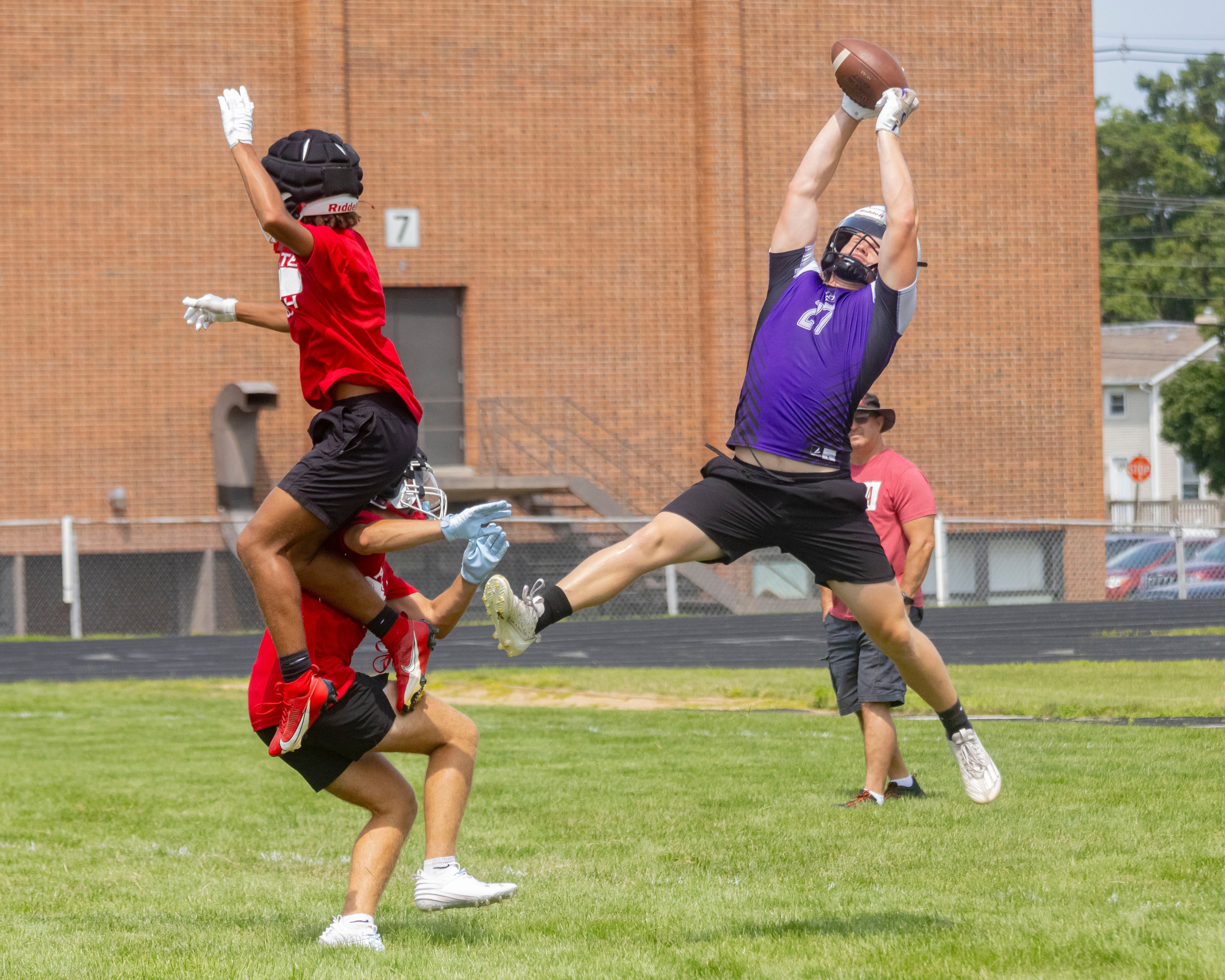 Eli Davidson of Dixon High School makes a leaping catch over two Ottawa High School defenders during a multiple high school practice football meet at Princeton High School on July 20, 2024.