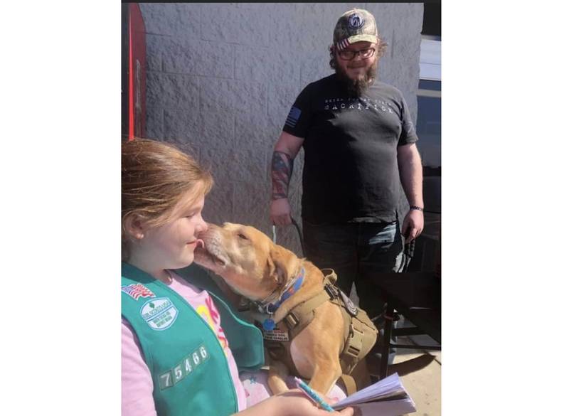 Bristol Sjostrom, 10, of Gardner, gets a big "kiss" from Rocky, the service dog of Zach Jett (right) of Coal City. In 2020, Girl Scout Troop 75466 in Mazon, of which Bristol is a member, sponsored Jett to receive a service dog to help with his post-traumatic stress disorder.